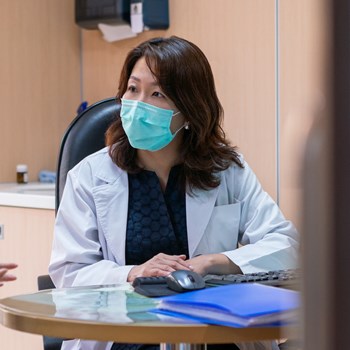 A doctor wearing a face mask sitting in front of a computer.