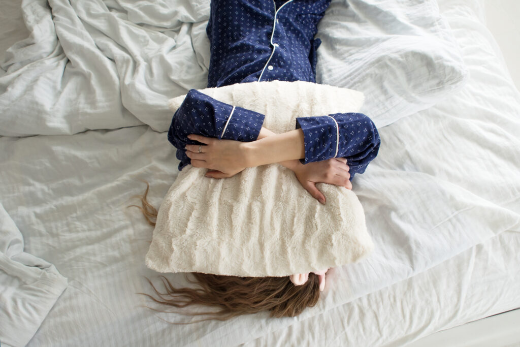 a woman laying on a bed hugging a pillow that is covering her face