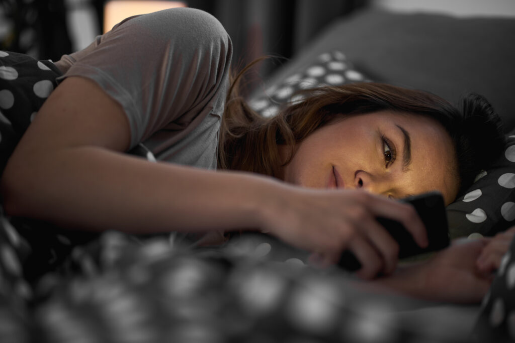 a woman laying in bed looking at her phone