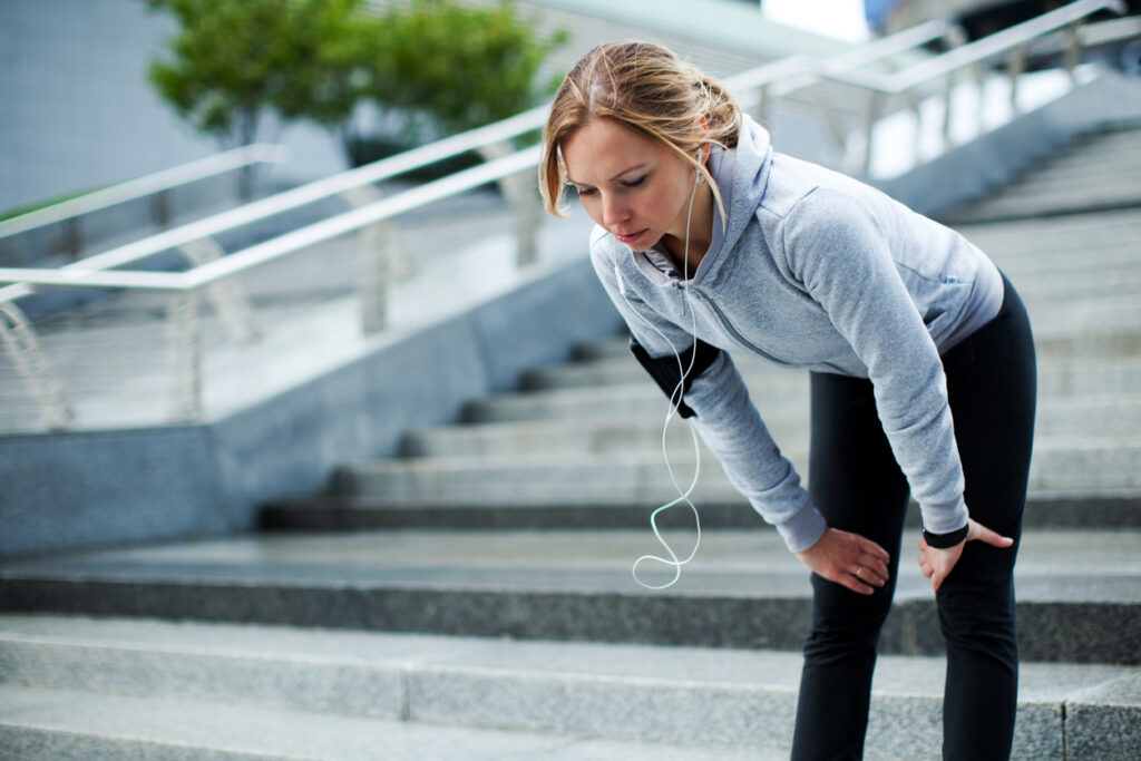 A woman with headphones in her ears bent over with her hands on her knees.